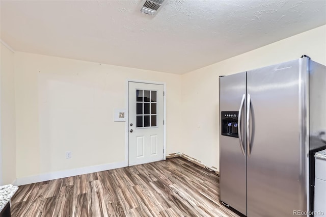 kitchen featuring wood finished floors, visible vents, baseboards, stainless steel fridge with ice dispenser, and a textured ceiling