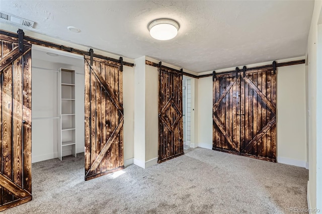 interior space featuring baseboards, visible vents, carpet floors, a textured ceiling, and a barn door