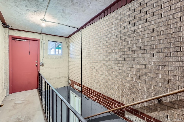 corridor featuring crown molding, unfinished concrete floors, brick wall, and a textured ceiling