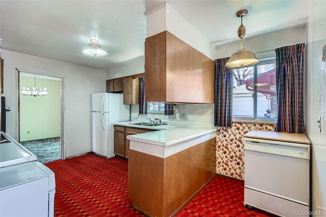 kitchen featuring a sink, decorative light fixtures, white appliances, a peninsula, and light countertops