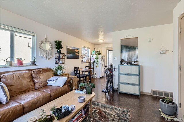 living room with dark wood-style floors, visible vents, and baseboards