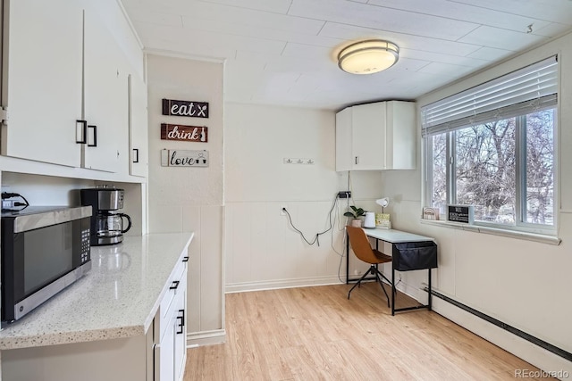 kitchen with light stone counters, light wood-style floors, white cabinetry, stainless steel microwave, and baseboard heating