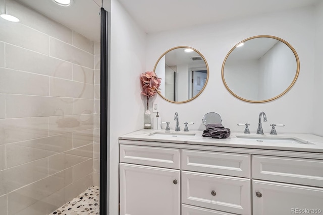 bathroom featuring double vanity, visible vents, tiled shower, and a sink