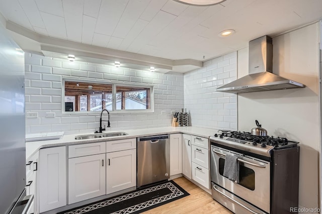 kitchen with light wood-style flooring, a sink, stainless steel appliances, wall chimney exhaust hood, and backsplash