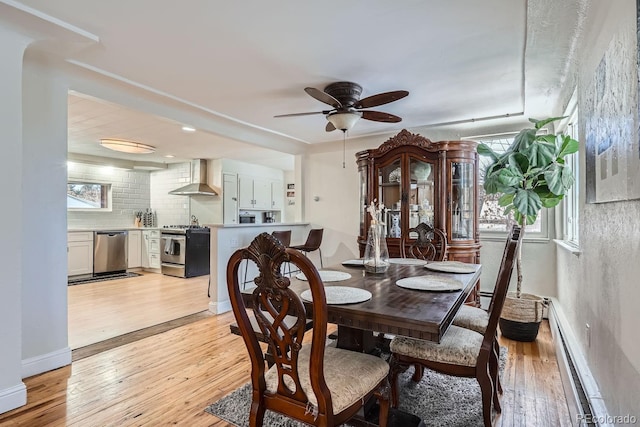 dining space with plenty of natural light, a ceiling fan, a baseboard heating unit, and light wood-style floors