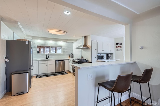 kitchen with a sink, appliances with stainless steel finishes, a peninsula, wall chimney range hood, and decorative backsplash