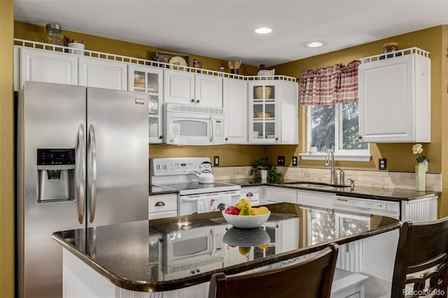 kitchen featuring white appliances, a sink, white cabinets, a center island, and glass insert cabinets