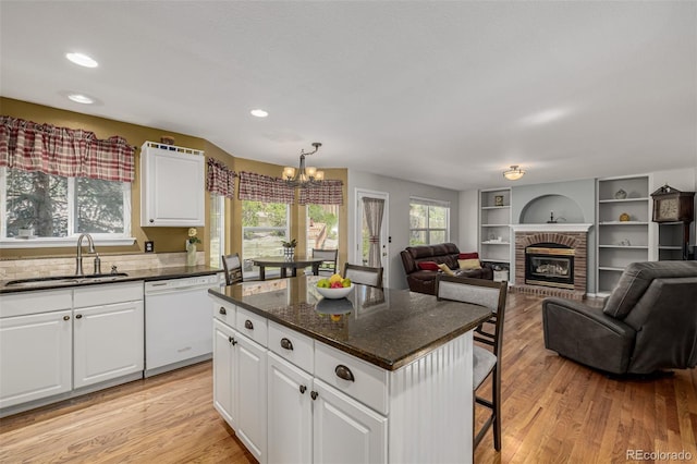 kitchen featuring a sink, white dishwasher, a chandelier, light wood-type flooring, and a kitchen bar