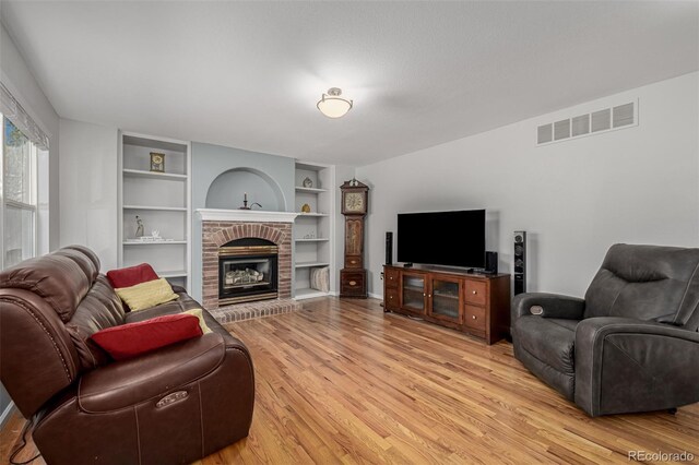 living area featuring light wood-style flooring, built in features, and a fireplace