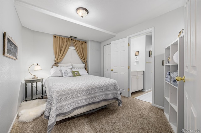bedroom featuring light carpet, baseboards, ensuite bath, and a closet