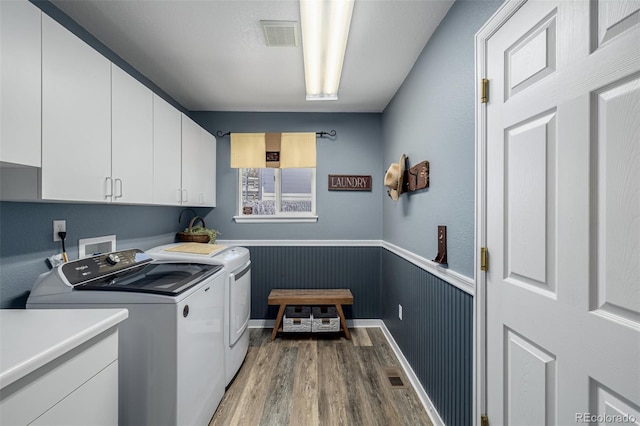 laundry area with cabinet space, separate washer and dryer, wood finished floors, and a wainscoted wall