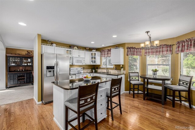 kitchen with white appliances, a sink, a chandelier, light wood-style floors, and white cabinets