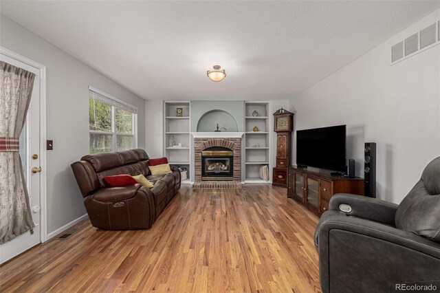 living room featuring light wood-type flooring, a brick fireplace, built in shelves, and baseboards