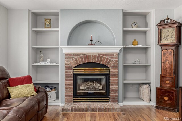 living area with built in shelves, wood finished floors, and a fireplace