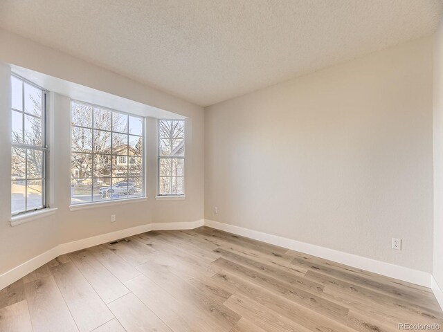 spare room with a textured ceiling and light hardwood / wood-style floors