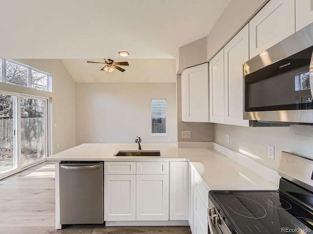 kitchen featuring kitchen peninsula, appliances with stainless steel finishes, sink, light hardwood / wood-style floors, and white cabinetry