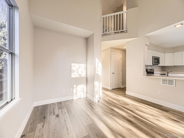 unfurnished living room with light wood-type flooring and a high ceiling