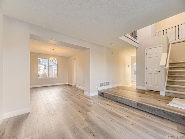 spare room featuring a chandelier, a textured ceiling, and light wood-type flooring