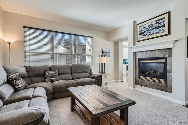 living area featuring a tile fireplace, light carpet, and baseboards