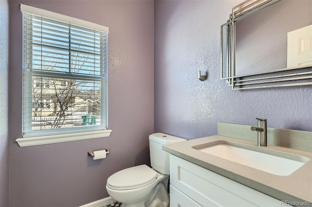 half bathroom featuring a textured wall, vanity, and toilet