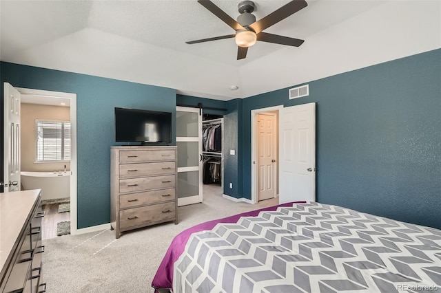 bedroom with light colored carpet, visible vents, a barn door, vaulted ceiling, and baseboards