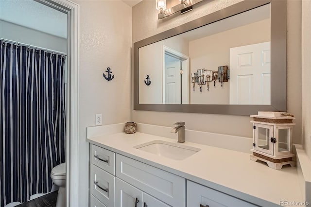 bathroom featuring toilet, a textured wall, and vanity