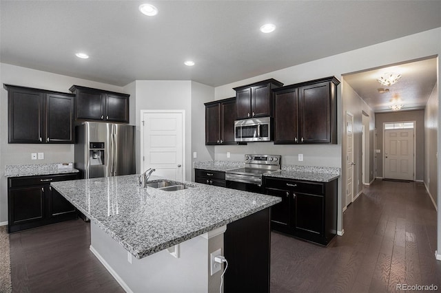 kitchen with light stone countertops, sink, dark wood-type flooring, a kitchen island with sink, and appliances with stainless steel finishes