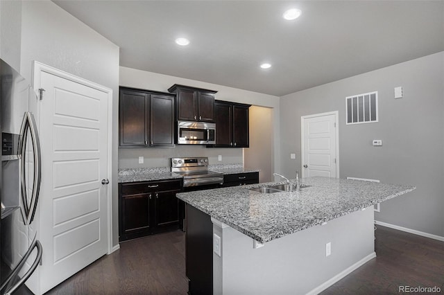 kitchen with dark brown cabinetry, sink, dark hardwood / wood-style flooring, an island with sink, and appliances with stainless steel finishes