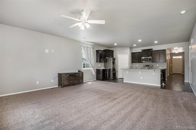 kitchen featuring ceiling fan, a kitchen breakfast bar, a kitchen island with sink, dark carpet, and appliances with stainless steel finishes