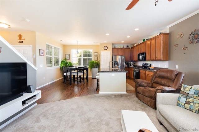 carpeted living area with wood finished floors, a sink, baseboards, ceiling fan, and recessed lighting