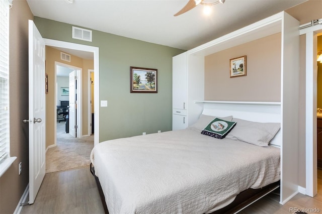 bedroom featuring a ceiling fan, baseboards, visible vents, and wood finished floors