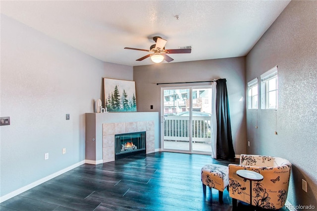 living area featuring plenty of natural light, ceiling fan, a textured ceiling, and a tiled fireplace