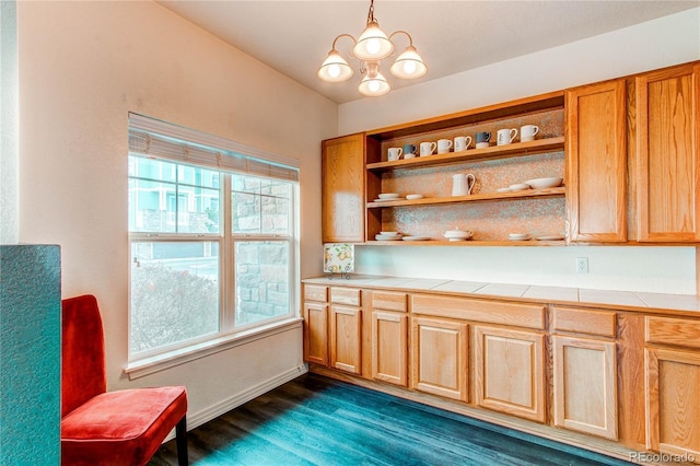 kitchen featuring vaulted ceiling, dark wood-type flooring, decorative light fixtures, a notable chandelier, and tile counters