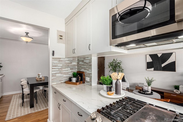 1454 Jersey St Unit 104, Denver, CO 80220 - kitchen featuring stainless steel microwave, light wood finished floors, backsplash, white cabinets, and cooktop