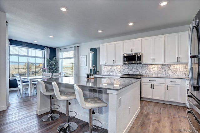 kitchen featuring a kitchen island with sink, stainless steel appliances, a sink, white cabinetry, and tasteful backsplash