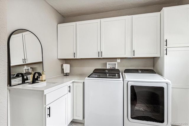 laundry area with washing machine and clothes dryer, cabinets, a textured ceiling, and sink