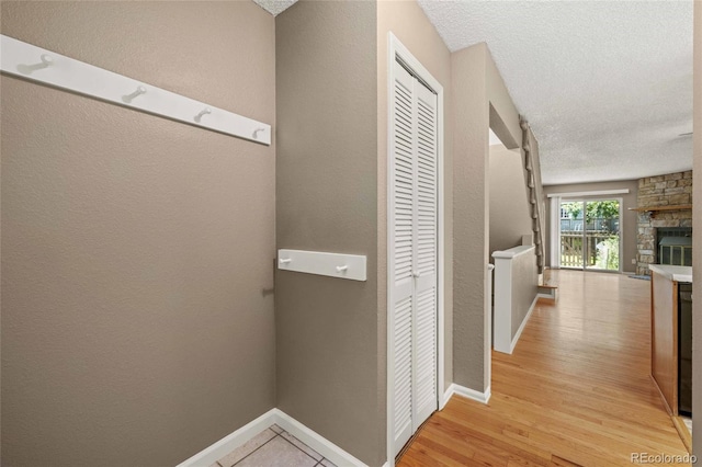 hallway featuring baseboards, a textured wall, a textured ceiling, and light wood finished floors