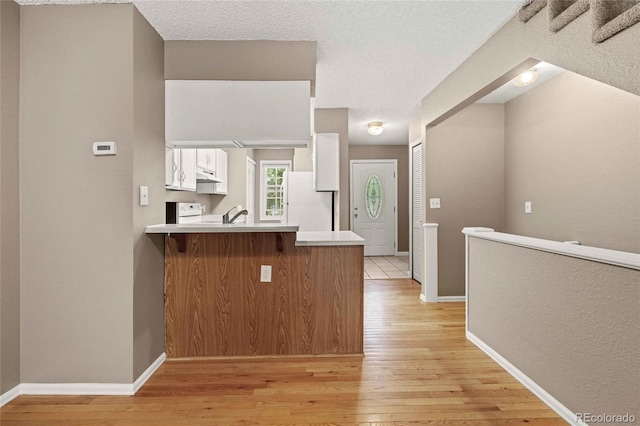 kitchen featuring a peninsula, white cabinetry, light wood-style floors, light countertops, and freestanding refrigerator