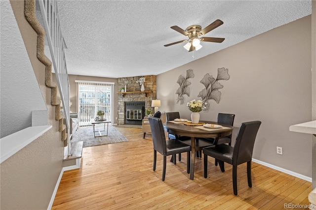 dining room with light wood-type flooring, baseboards, a stone fireplace, and a textured ceiling