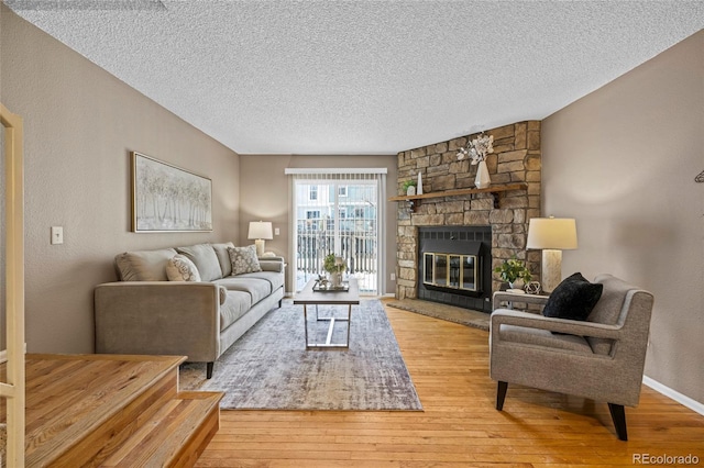 living area featuring a textured ceiling, light wood finished floors, a fireplace, and baseboards