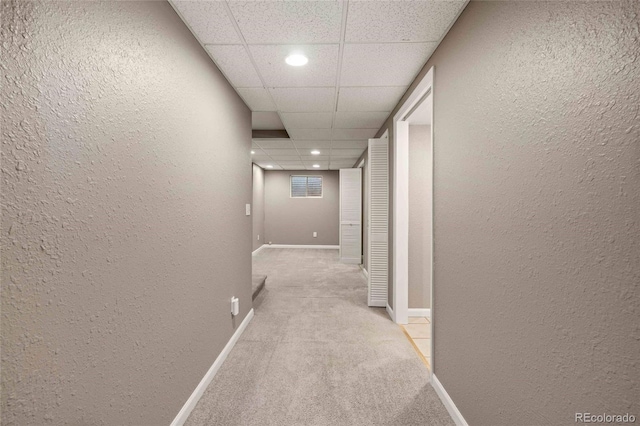 hallway featuring baseboards, a textured wall, and light colored carpet