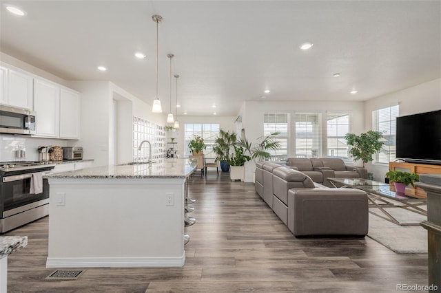 kitchen featuring white cabinetry, light stone counters, a center island with sink, appliances with stainless steel finishes, and pendant lighting