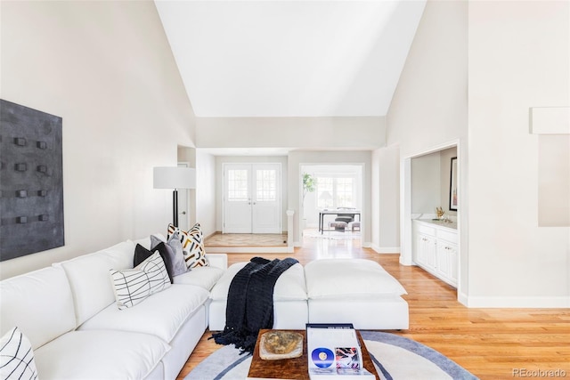living area with high vaulted ceiling, baseboards, and light wood-type flooring