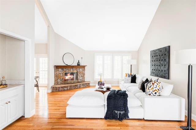 living area with high vaulted ceiling, baseboards, a fireplace, and light wood finished floors