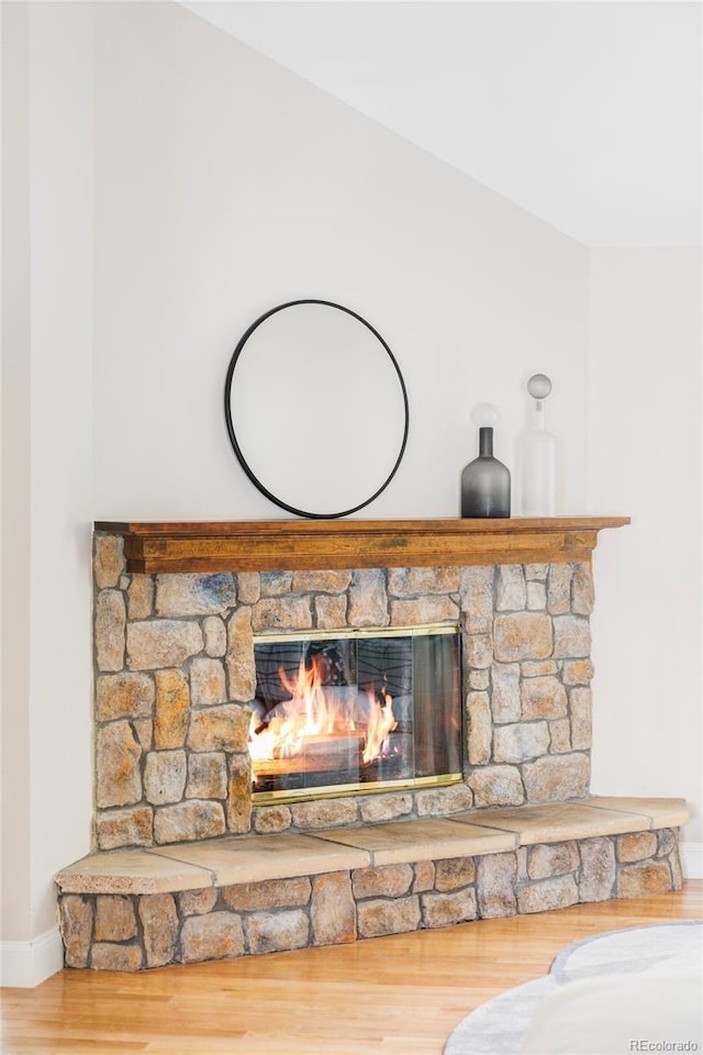details featuring baseboards, a stone fireplace, and wood finished floors