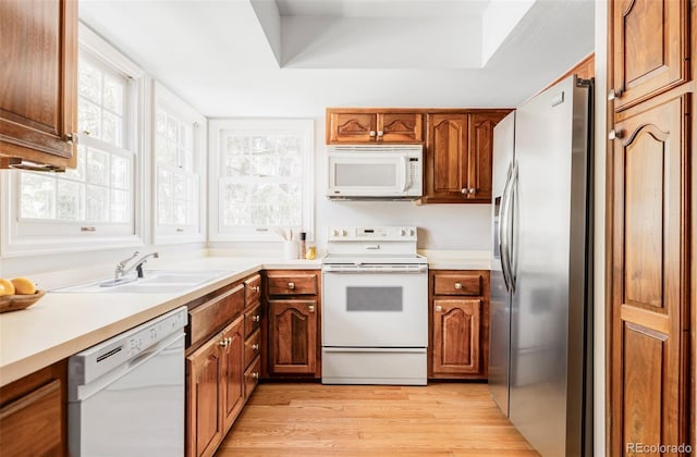 kitchen featuring brown cabinetry, a sink, white appliances, and light countertops