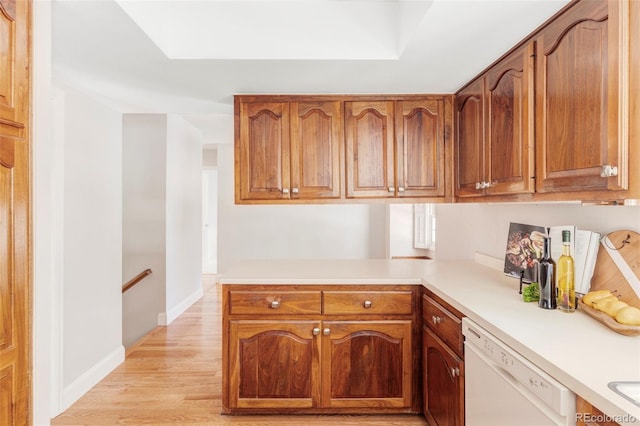 kitchen with white dishwasher, brown cabinets, light wood-type flooring, light countertops, and baseboards