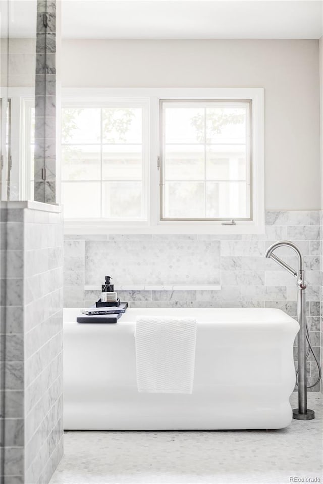 bathroom with a freestanding tub, tile walls, and a wealth of natural light