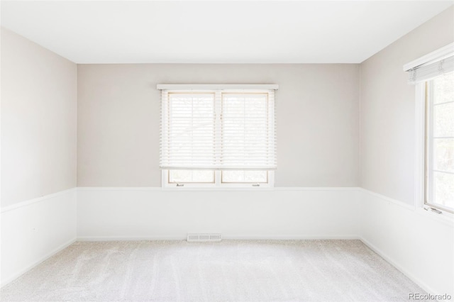 spare room featuring light colored carpet, a healthy amount of sunlight, and visible vents