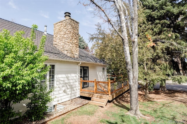 exterior space with a shingled roof, a wooden deck, and a chimney